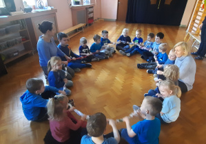 grupa dzieci ubrana na niebiesko siedzi w dużym kole na sali gimnastycznej
