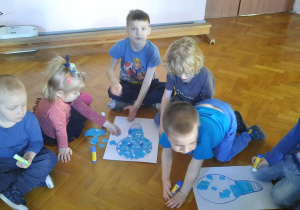 grupa dzieci ubrana na niebiesko wykleja kontur żarówki na sali gimnastycznej
