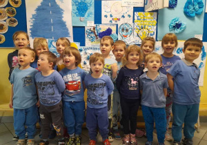 grupa dzieci ubrana na niebiesko pozuje do zdjęcia na tle plakatów
