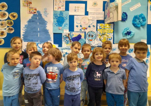 grupa dzieci ubrana na niebiesko pozuje do zdjęcia na tle plakatów