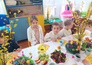 dzieci siedzą przy stolikach, na których widać świąteczne dekoracje, kolorowe serwetki, smakołyki na talerzach