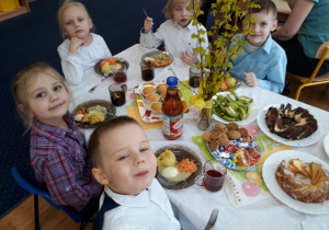Dzieci siedzą przy stole na którym są smakołyki i świąteczny obiad.