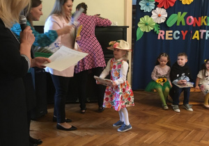 Dziewczynka odbiera nagrodę za udział w konkursie recytatorskim.