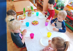 dzieci siedzą przy stoliku nakrytym białym obrusem, częstują się słodyczami