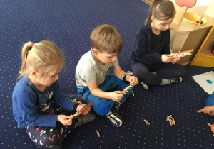 Dzieci siedzą na dywanie i przypinają klamerki do kartoników na których są napisane cyfry.