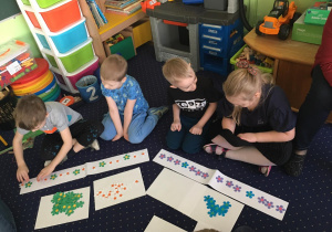 Dzieci siedzą na dywanie i układają rytmy z kwiatków.