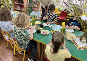 Dzieci siedzą przy stole i obierają swoje jajka.