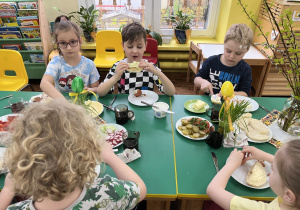Dzieci siedzą przy stole i zjadają śniadanie.