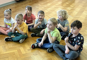 Dzieci siedzą na podłodze i słuchają muzyki.