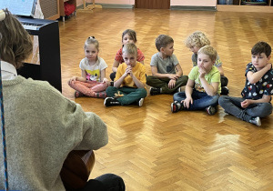 Dzieci siedzą na podłodze i słuchają muzyki.