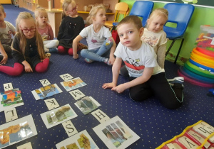 Dzieci siedzą w kole na dywanie, a przed nimi ilustracje dzikich zwierząt.