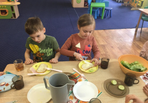 Dzieci siedzą przy stole i komponują kanapki.