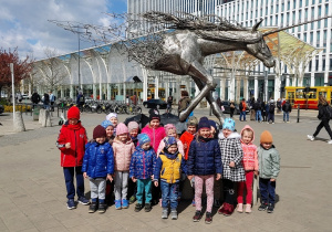 grupa dzieci pozuje do zdjęcia, dzieci stoją na chodniku, w tle widać pomnik Jednorożca.