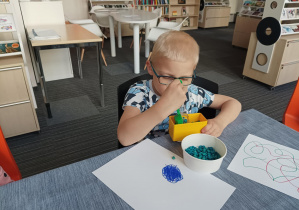 chłopiec przy dużym stole wkłada kolorowe kulki soczewicy do tekturowej formy