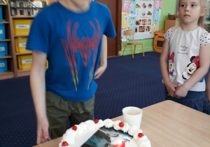 Chłopiec stoi przy stole i zdmuchuje świeczkę z tortu.