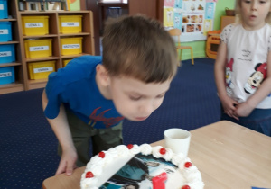 Chłopiec stoi przy stole i zdmuchuje świeczkę z tortu.