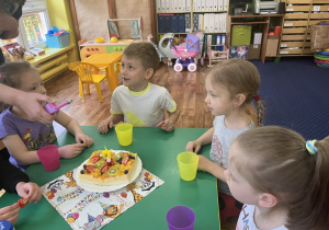 Dzieci siedzą przy stole na którym stoi ciasto.