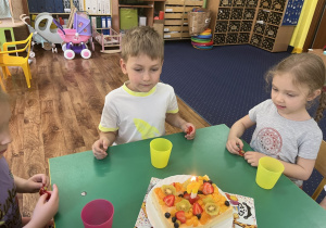 Dzieci siedzą przy stole, przed solenizantem stoi tort ze świeczką.