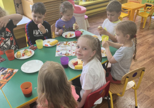 Dzieci siedzą przy stole i zjadają słodki poczęstunek.