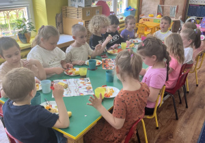 Dzieci siedzą przy stole i zjadają słodki poczęstunek.
