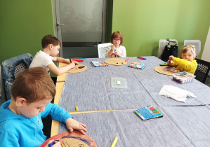 dzieci siedzą przy dużym stole, rysują mazakami
