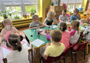 Dzieci siedzą przy stole na którym znajdują się słodkości.