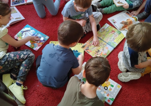 grupa dzieci na zajęciach w bibliotece, siedzą na podłodze, oglądają książki
