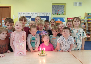 grupa dzieci stoi za stolikiem, na nim widać zabawkowy tort z cyfrą 5 i świeczkami