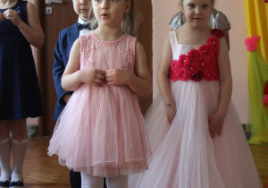 dwie dziewczynki w odświętnych sukienkach na sali gimnastycznej prezentują wiersz dla rodziców