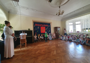 Dzieci i dorośli słuchają piosenki śpiewanej przez Szymona.