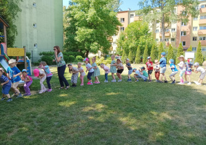 dzieci stoją w dużym kole w ogródku przedszkolnym, tańczą, śpiewają