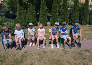 grupa dzieci siedzi na ławce w ogrodzie przedszkolnym