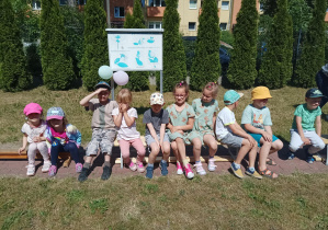 grupa dzieci siedzi na ławce w ogrodzie przedszkolnym