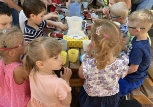 dzieci siedzą przy stole piknikowym na tarasie przedszkolnym, jedzą owoce i słodkie przekąski