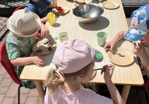 dzieci siedzą przy stole piknikowym na tarasie przedszkolnym, jedzą owoce i słodkie przekąski
