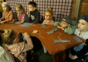Dzieci siedzą przy stole i wykonują lalki ze szmatek.
