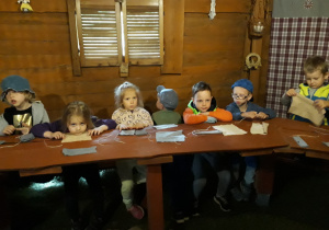 Dzieci siedzą przy stole i wykonują lalki ze szmatek.