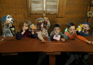 Dzieci siedzą przy stole i prezentują swoje lalki ze szmatek.