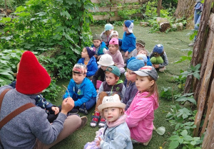 dzieci na wycieczce w dolinie skrzatów zwiedzają razem ze skrzatologiem w czerwonej czapce