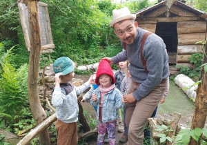 dzieci na wycieczce w dolinie skrzatów zwiedzają razem ze skrzatologiem w czerwonej czapce