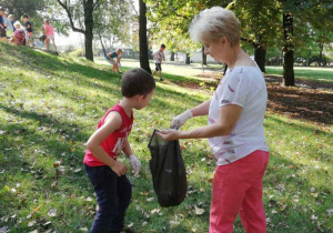 Dorośli i dzieci zbierają śmieci w parku.