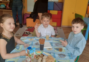 Troje dzieci siedzi przy stoliku i zjada słodki poczęstunek.