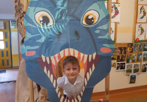 Chłopiec pozuje w paszczy dinozaura - dekoracji.