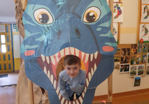 Chłopiec pozuje w paszczy dinozaura - dekoracji.