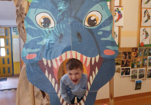 Chłopiec pozuje z groźną miną w paszczy dinozaura - dekoracji.