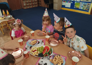 dzieci świętują urodziny koleżanek, na stolikach widać kolorowe serwetki, napoje, słodycze