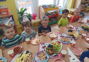 dzieci świętują urodziny koleżanek, na stolikach widać kolorowe serwetki, napoje, słodycze