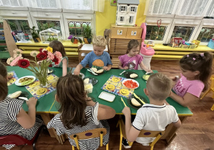 Dzieci siedzą przy stole i przygotowują sobie kanapki.