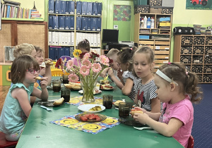 Dzieci siedzą przy stole, przygotowują sobie kanapki i je zjadają.