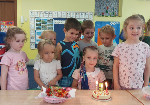 dziewczynka świętuje urodziny, dzieci stoją za stołem, na którym widać symboliczny tort